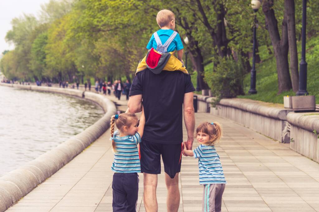 Man walking with his two daughters either side of him and his youngest child on his shoulders.